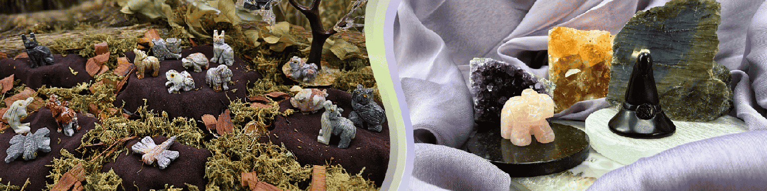 A collection of carved animal figures displayed on a natural earth-like background with a gemstone tree. On the left, there is an elephant carving on a polished black stone slice, along with a witch hat carving placed on a white stone and another stone slice beside it. Druzy stones are arranged in the background.